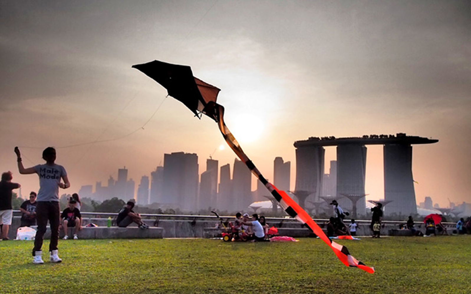Person flying a kite at sunset with Singapore skyline in the background.